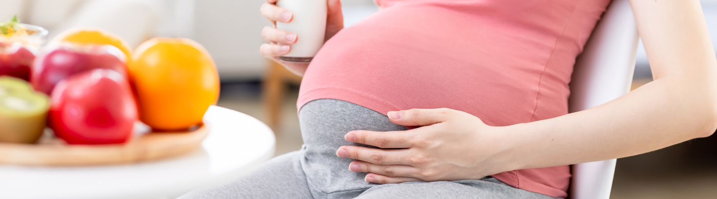 Mujer embarazada en ropa cómoda sonriendo mientras toma un batido de proteínas, en un entorno luminoso y natural