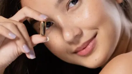 Mujer joven sosteniendo un suplemento deportivo para principiantes en cápsula cerca del rostro, representando el inicio en el mundo de la suplementación.