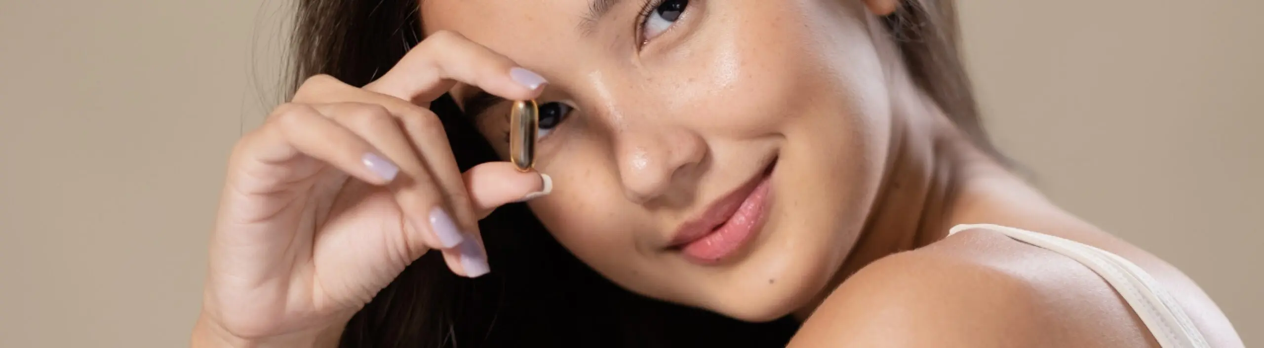 Mujer joven sosteniendo un suplemento deportivo para principiantes en cápsula cerca del rostro, representando el inicio en el mundo de la suplementación.