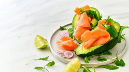 Plato de dieta keto con aguacate relleno de salmón ahumado, rúcula y aros de cebolla cruda