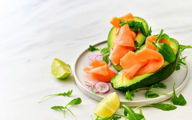 Plato de dieta keto con aguacate relleno de salmón ahumado, rúcula y aros de cebolla cruda