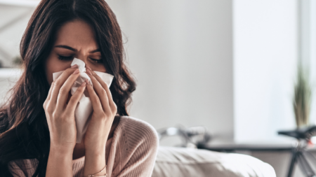 Persona con resfriado tomando medicamentos y bebiendo té caliente con limón y miel.