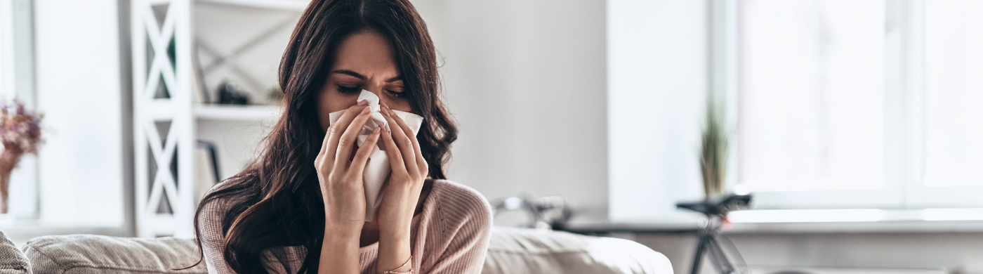 Persona con resfriado tomando medicamentos y bebiendo té caliente con limón y miel.