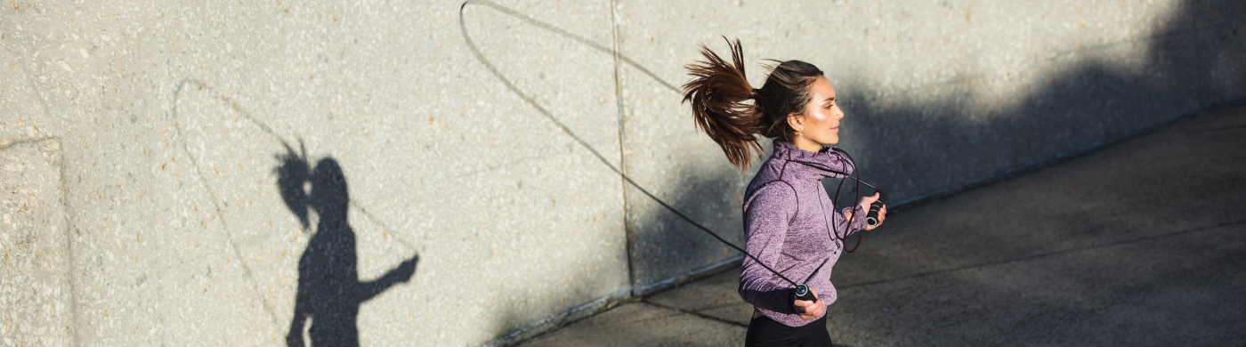 Persona saltando la cuerda al aire libre, destacando beneficios como mejora cardiovascular, quema de calorías y fortalecimiento muscular.